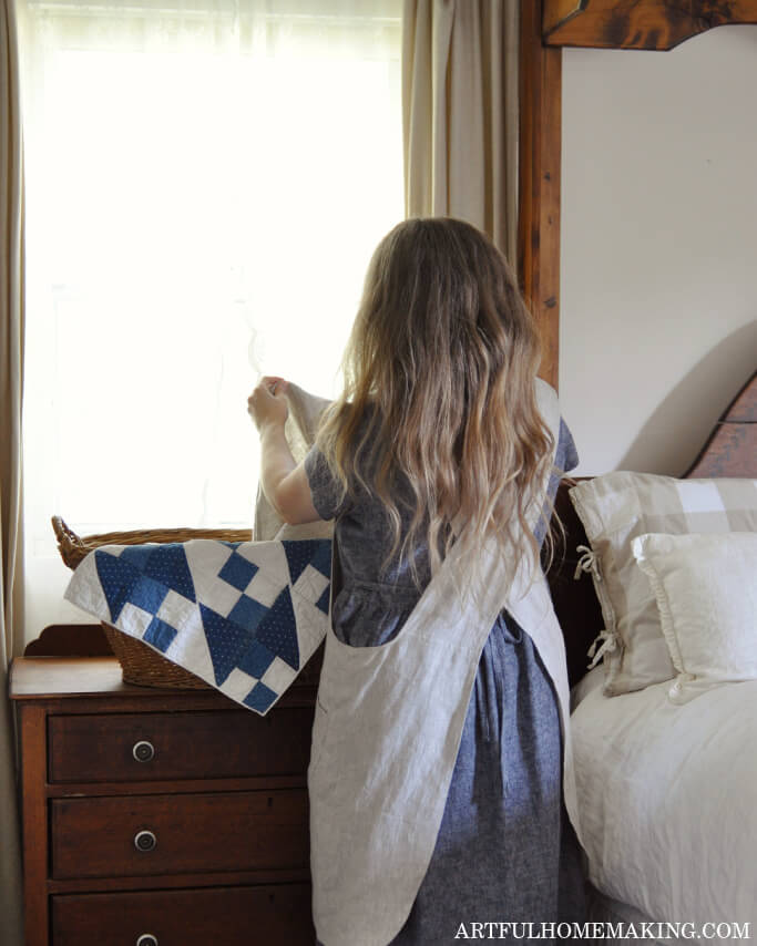 woman in a blue linen dress and natural linen apron folding laundry