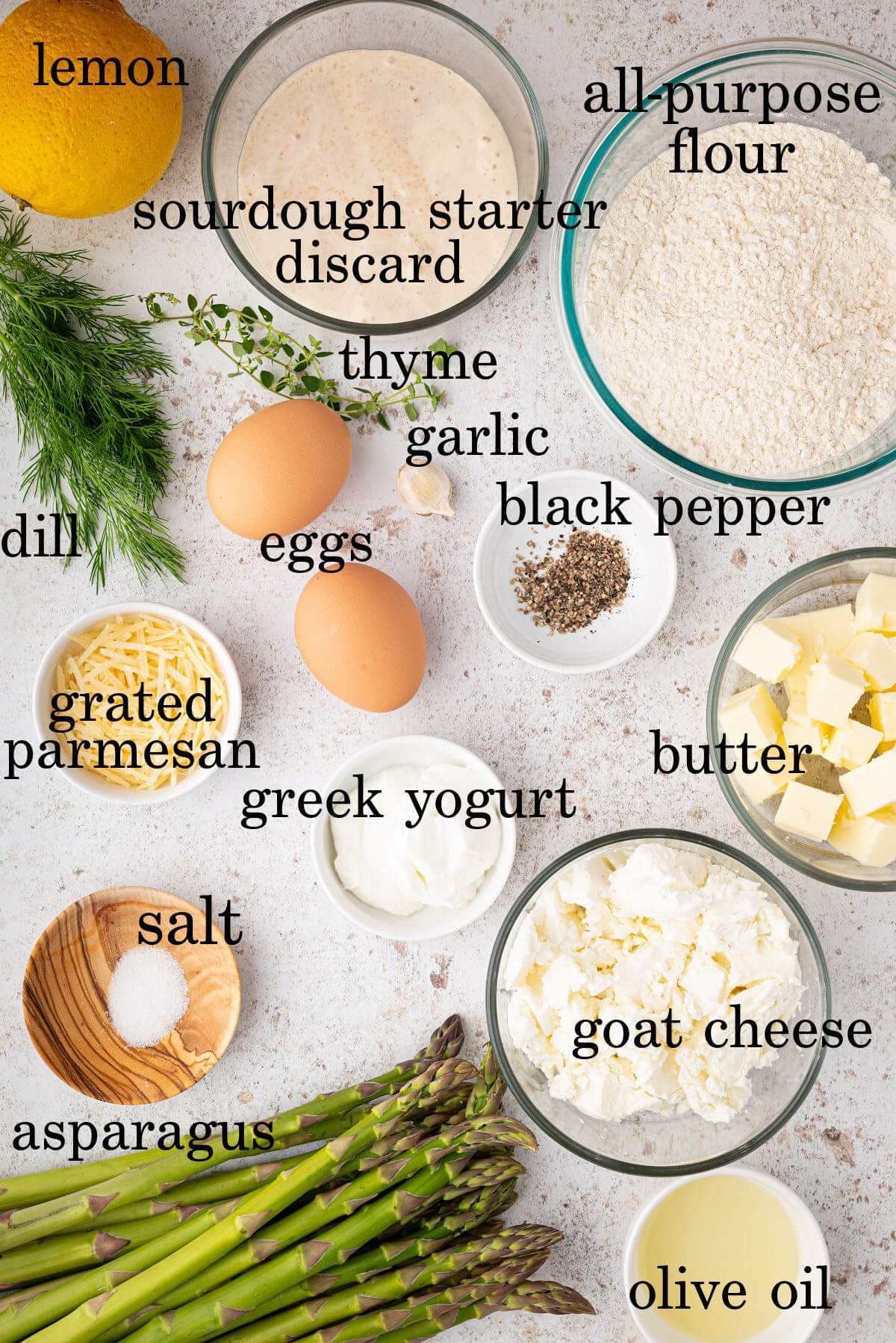 Ingredients for asparagus goat cheese tart in small bowls with text overlay labeling each ingredient.