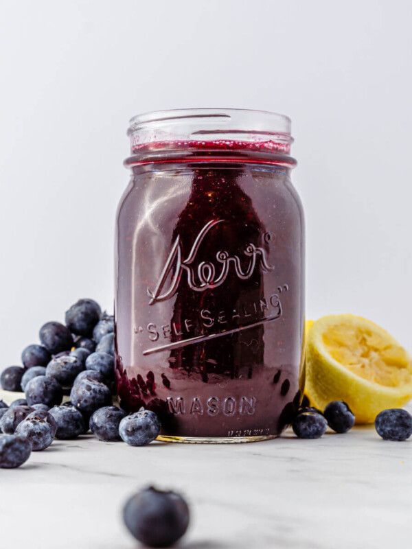 Blueberry syrup in a mason jar with a pile of blueberries next to it.
