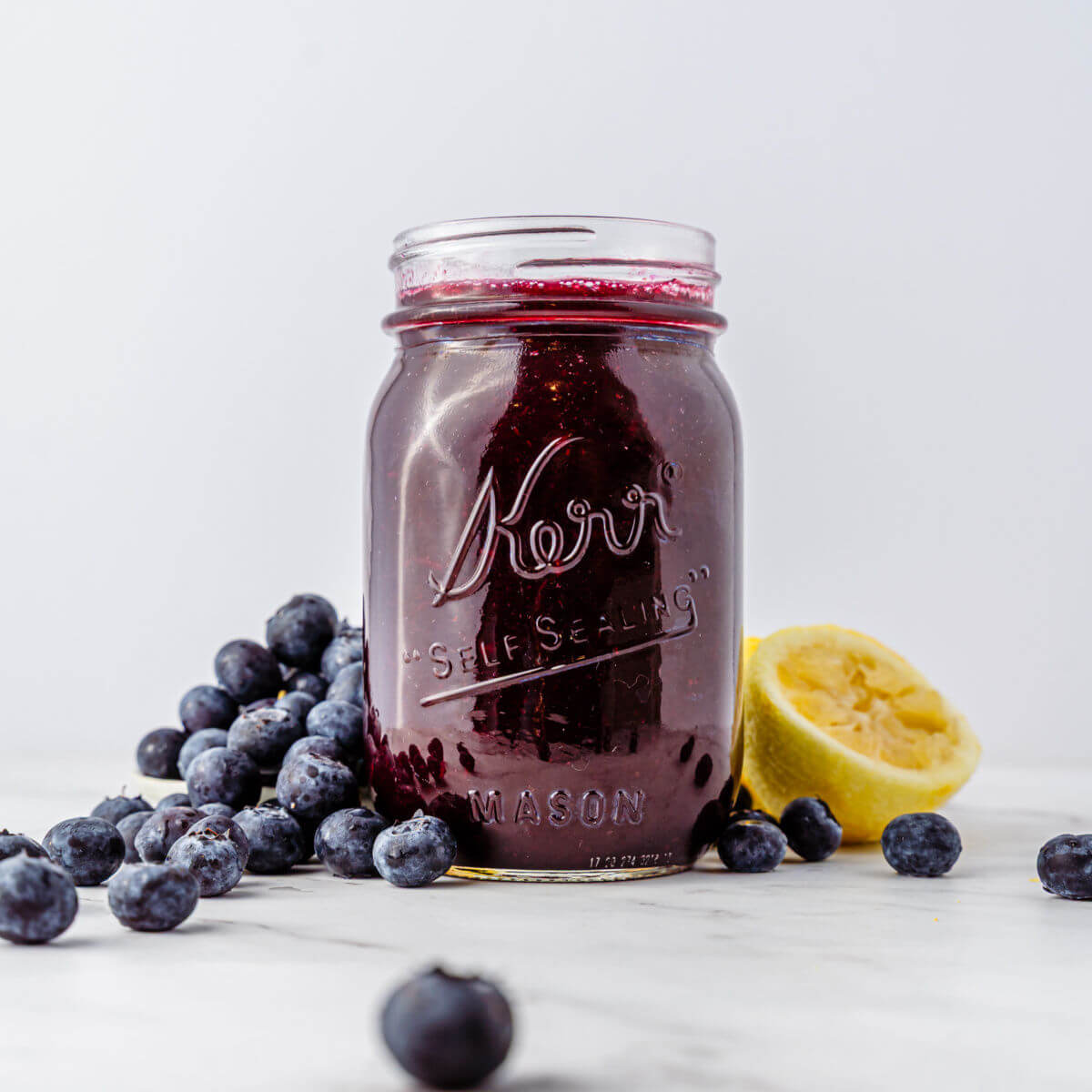 Blueberry syrup in a mason jar with a pile of blueberries next to it.
