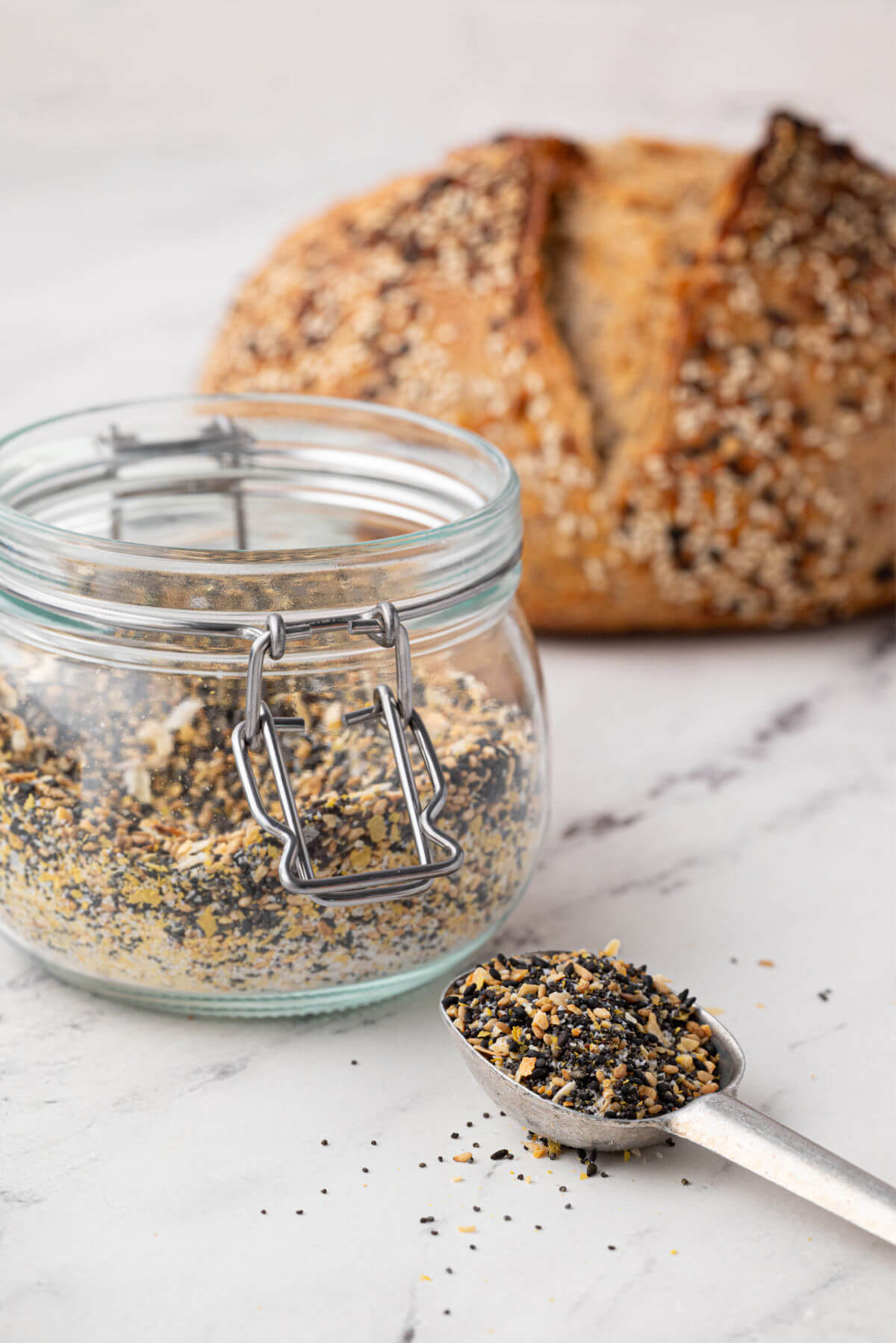 A jar and measuring spoon filled with everything bagel seasoning mix.
