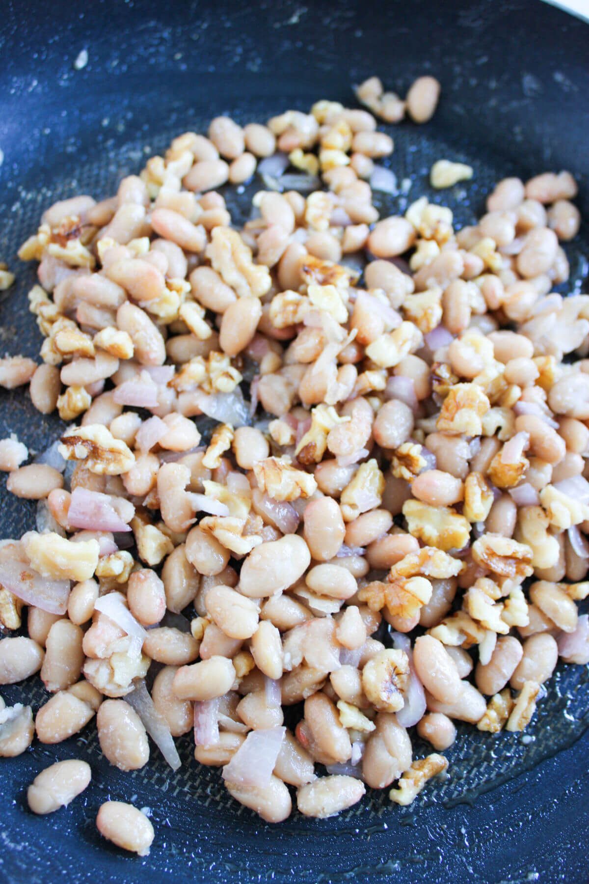 Butter beans, shallots, and walnuts being cooked in olive oil.