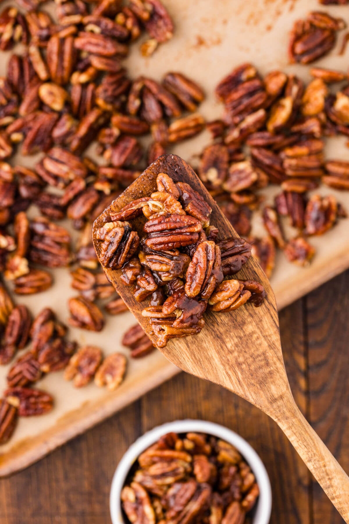A wooden spoon holding up a spoonful of candied maple pecans.