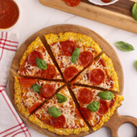 Cauliflower pizza crust on a round cutting board.