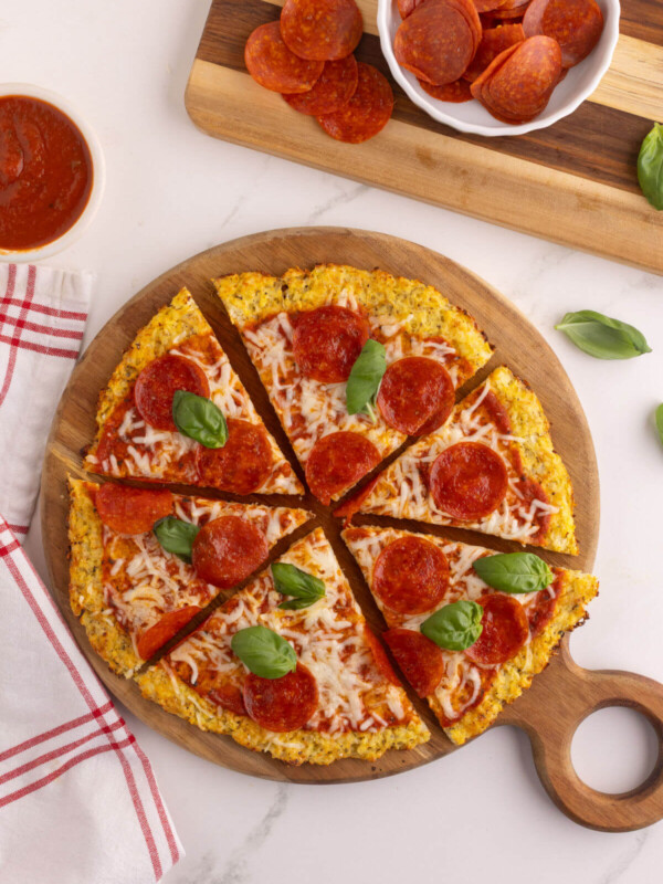 Cauliflower pizza crust on a round cutting board.