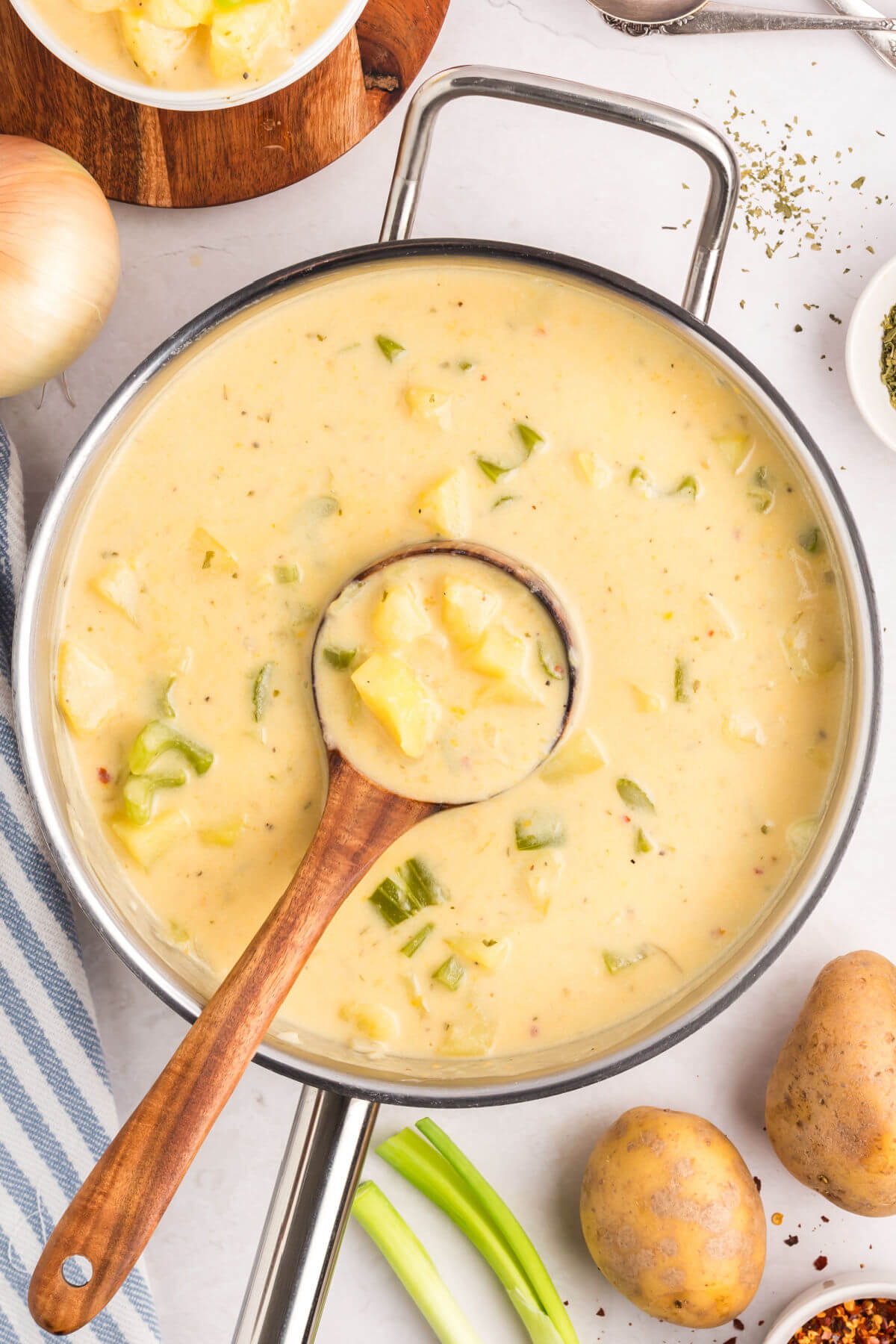 top down view of cheesy potato soup in a pot with a wooden spoon