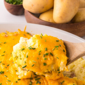a wooden spoon removing mashed potato casserole from a dish