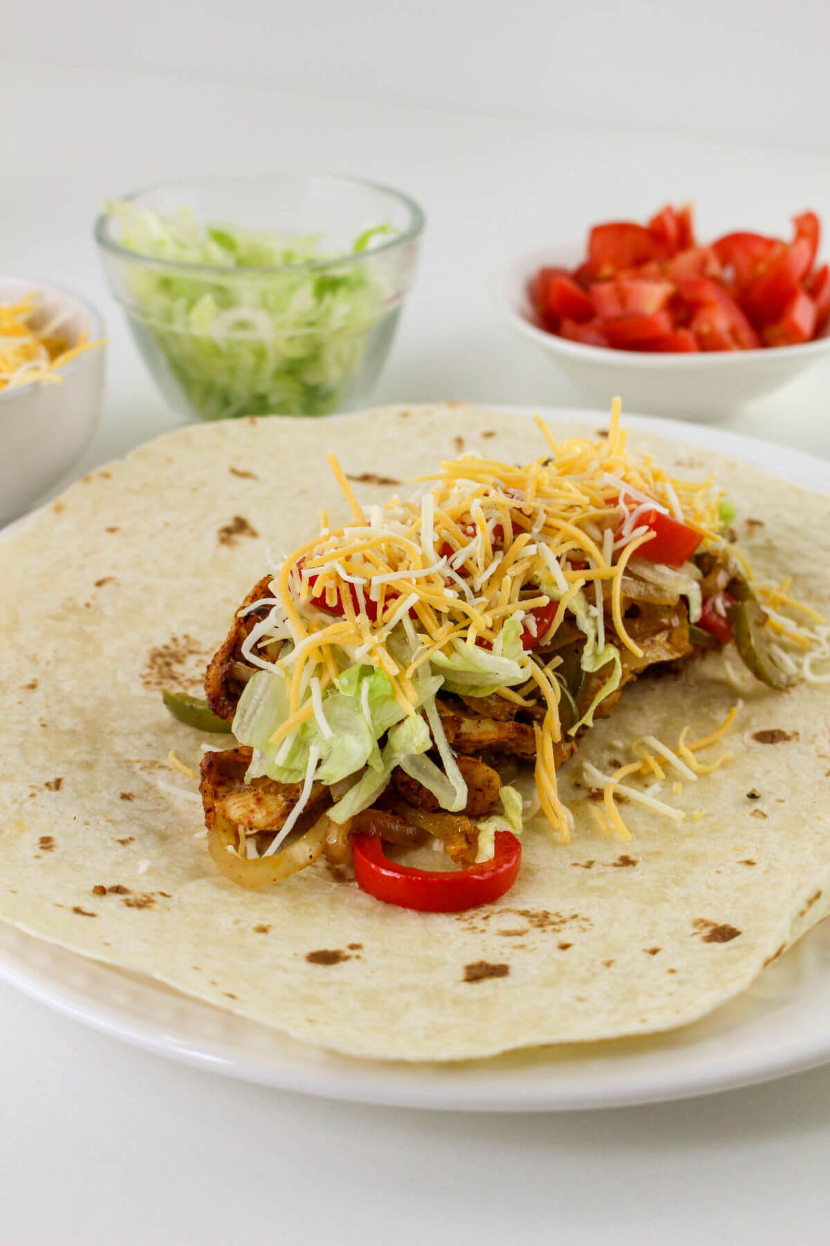 Adding cooked chicken fajita filling and cheese to a tortilla.
