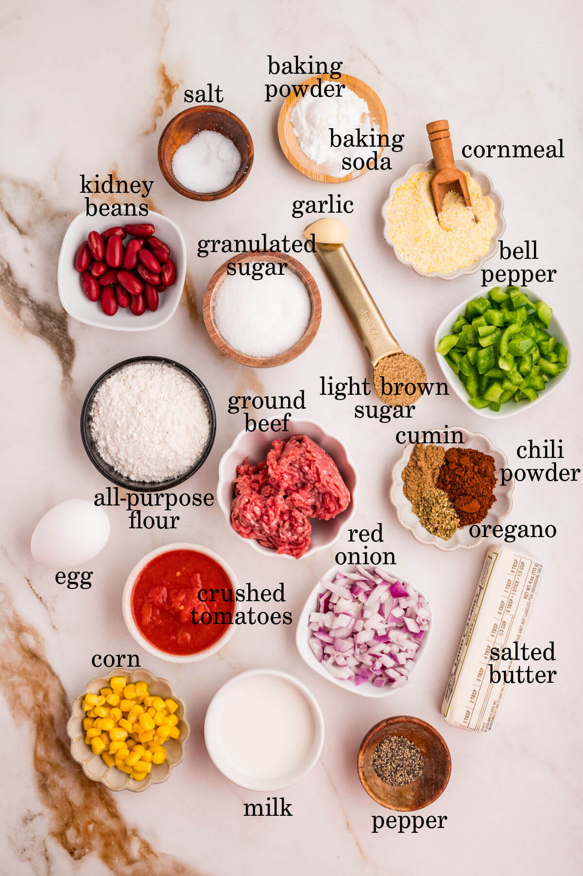 Ingredients for chili cornbread casserole in small bowls with text overlay labeling each ingredient.