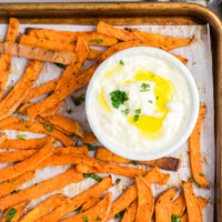 Crispy sweet potato fries with garlic aioli sauce on a sheet pan.