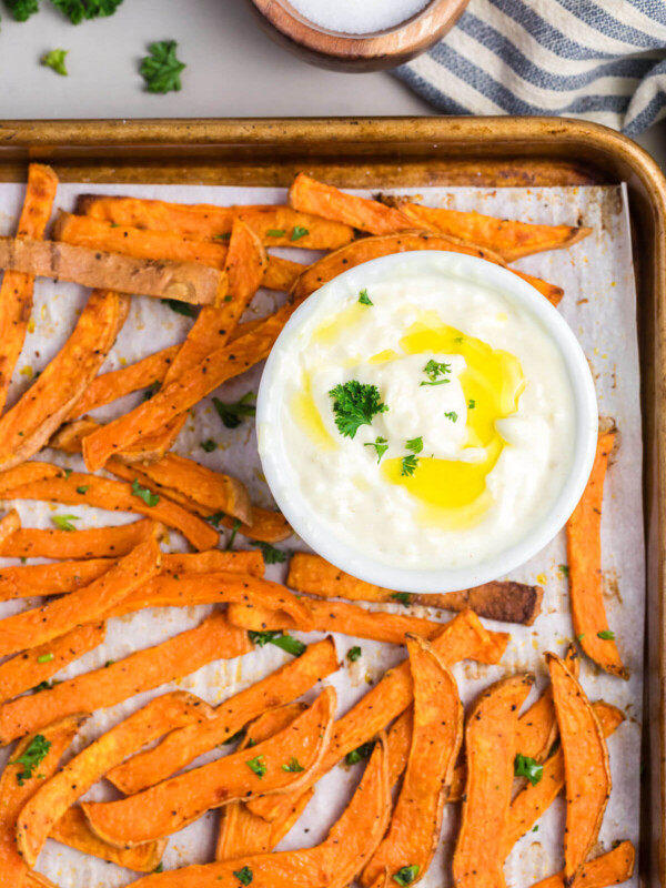 Crispy sweet potato fries with garlic aioli sauce on a sheet pan.