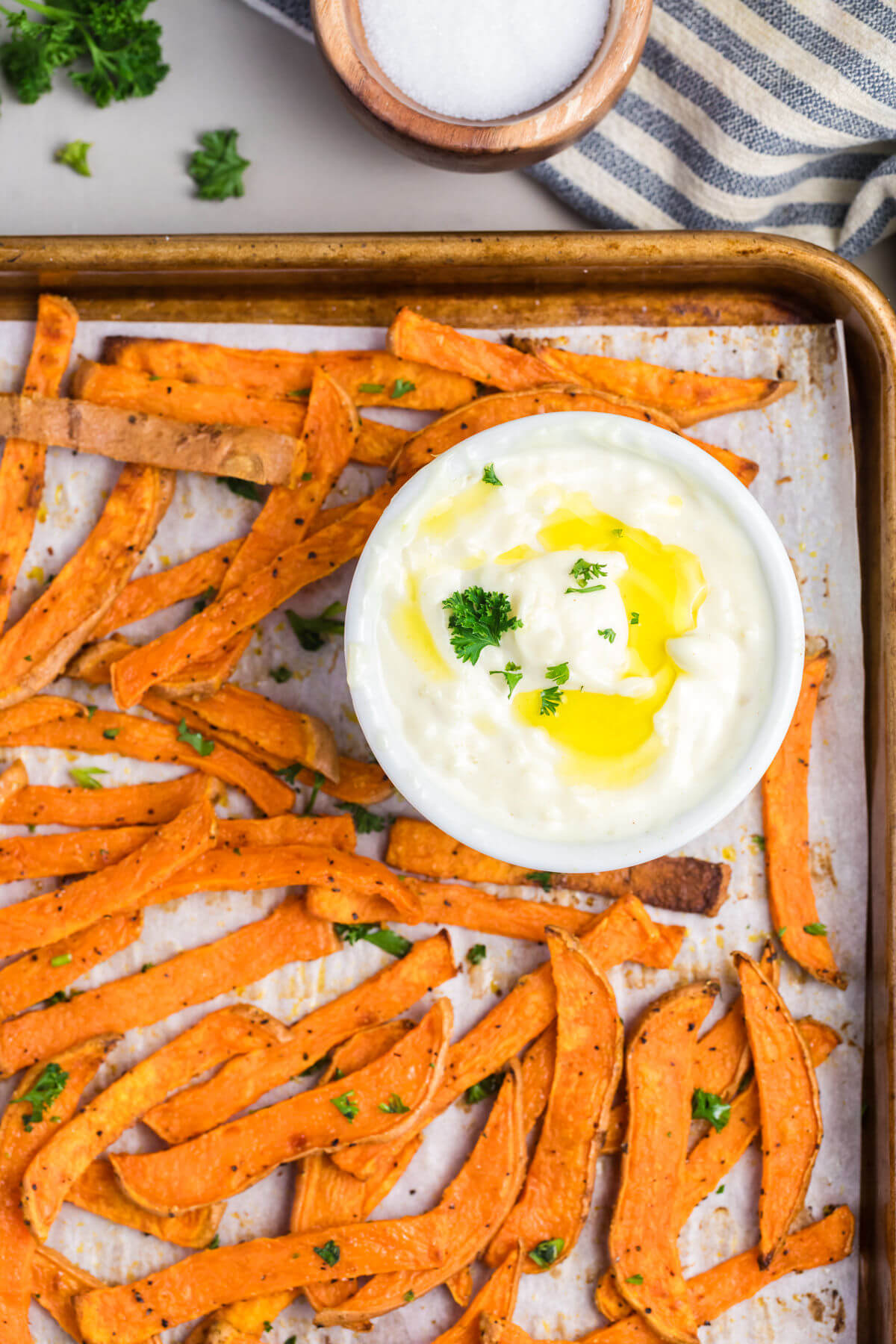 Crispy sweet potato fries with garlic aioli sauce on a sheet pan.
