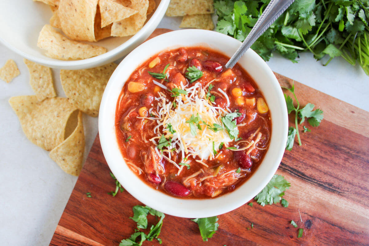 Crockpot chicken taco chili in a bowl with shredded cheese, parsley, and tortilla chips.