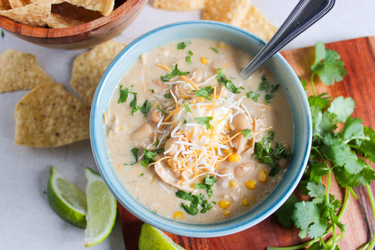 Creamy crockpot white chicken chili in a bowl with lime wedges and parsley.