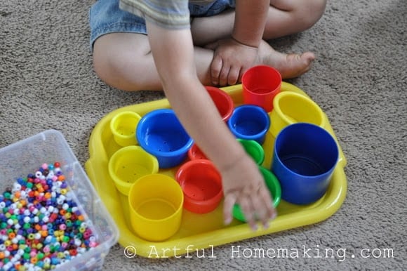 toddler playing with stacking cups and pony beads