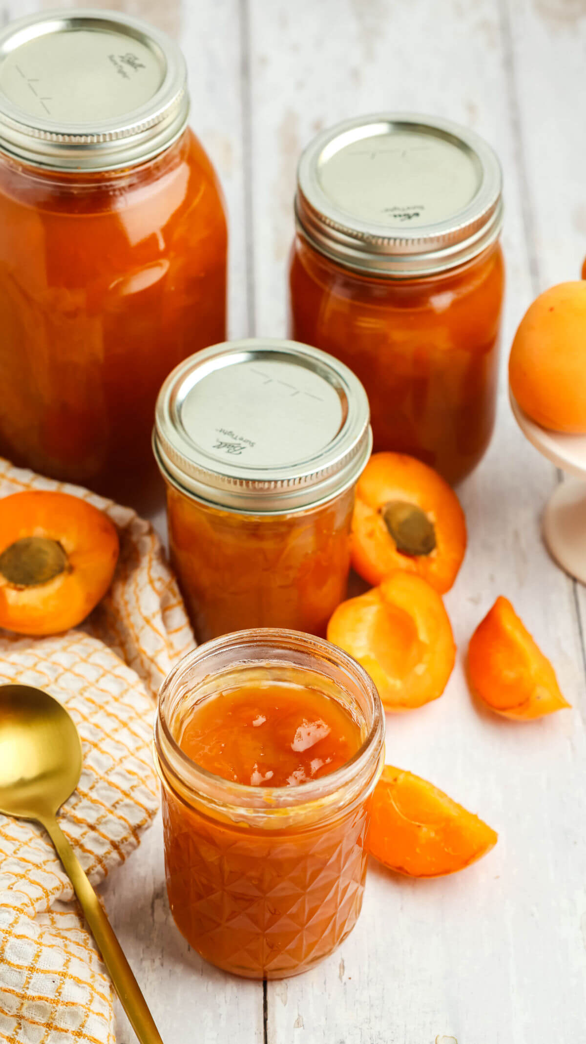 Jars of apricot jam surrounded by halved apricots.