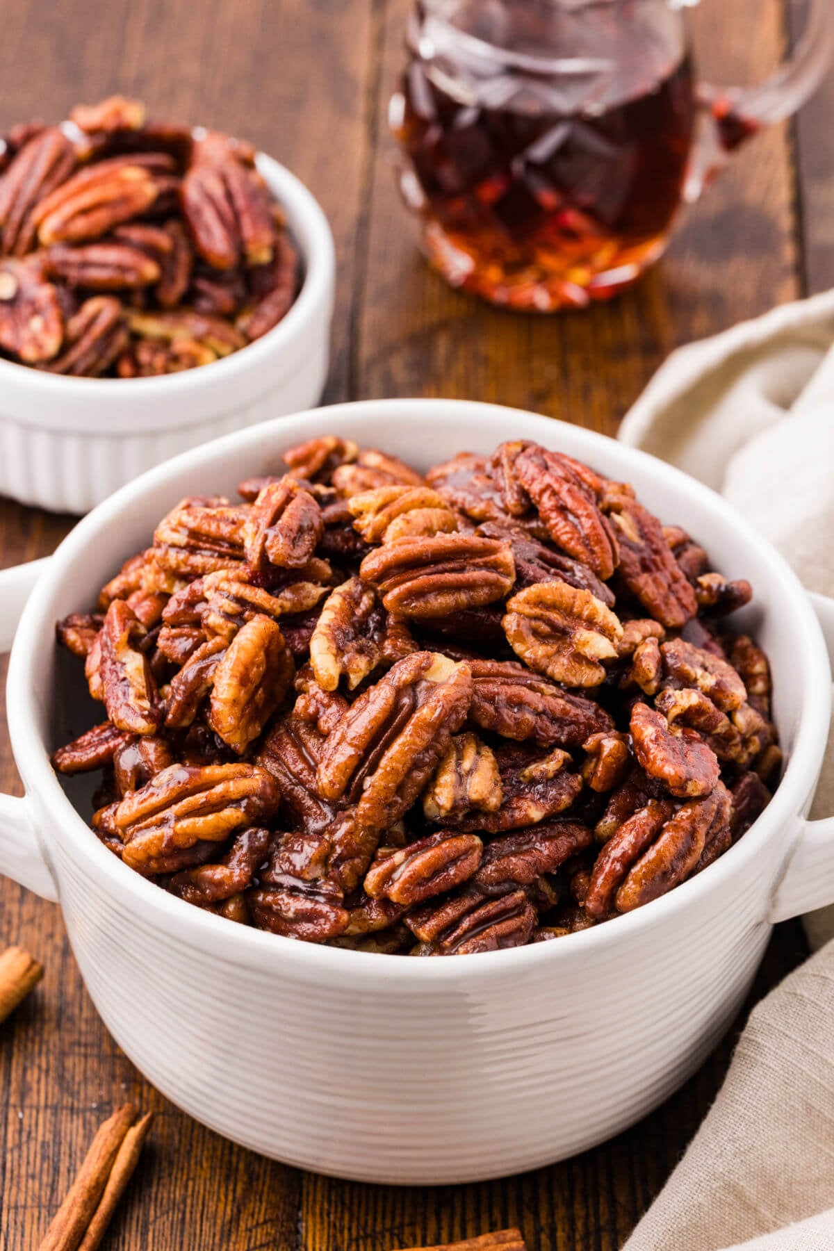 A bowl with candied maple pecans and a jar of maple syrup.