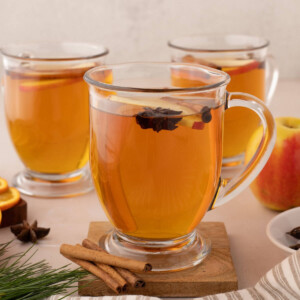Three clear glass mugs of hot spiced apple cider from apple juice.