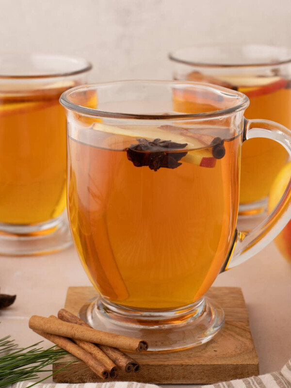 Three clear glass mugs of hot spiced apple cider from apple juice.