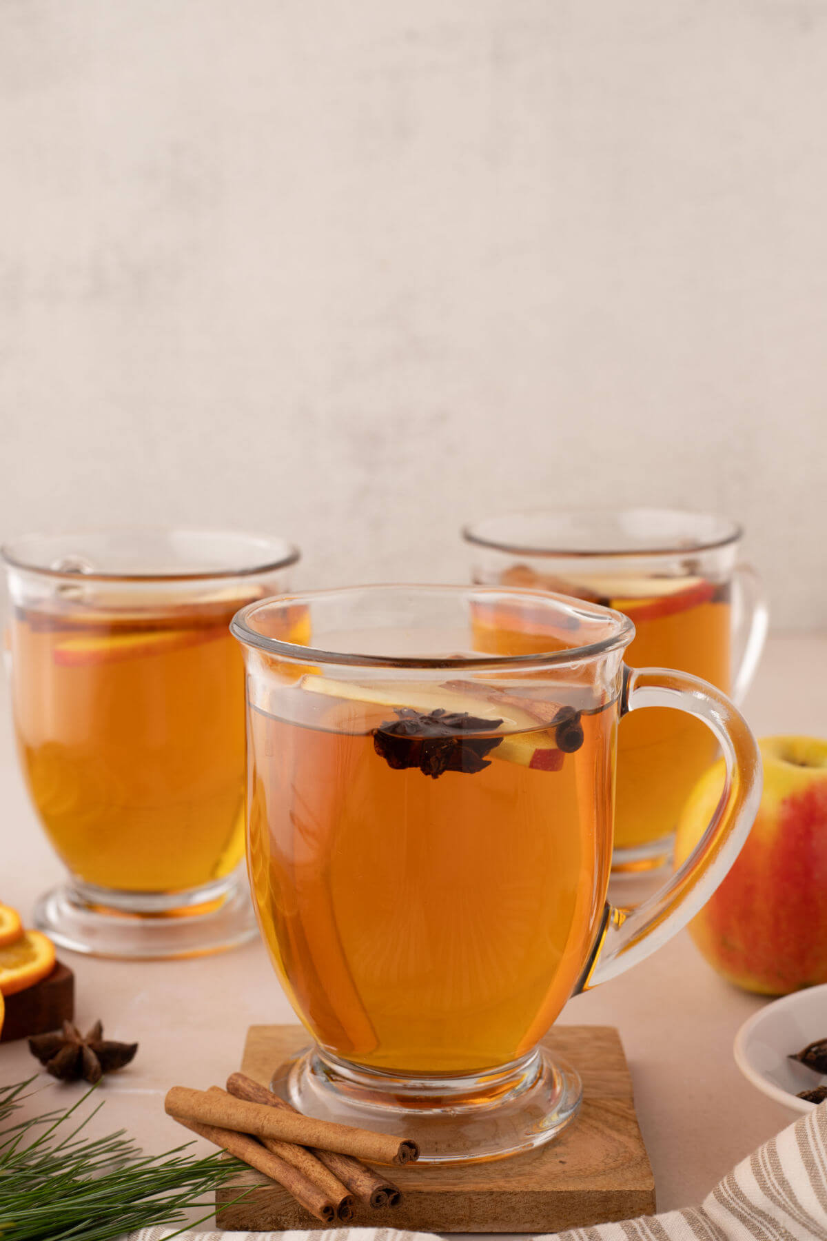Three clear glass cups with apple cider from apple juice and seasonings.