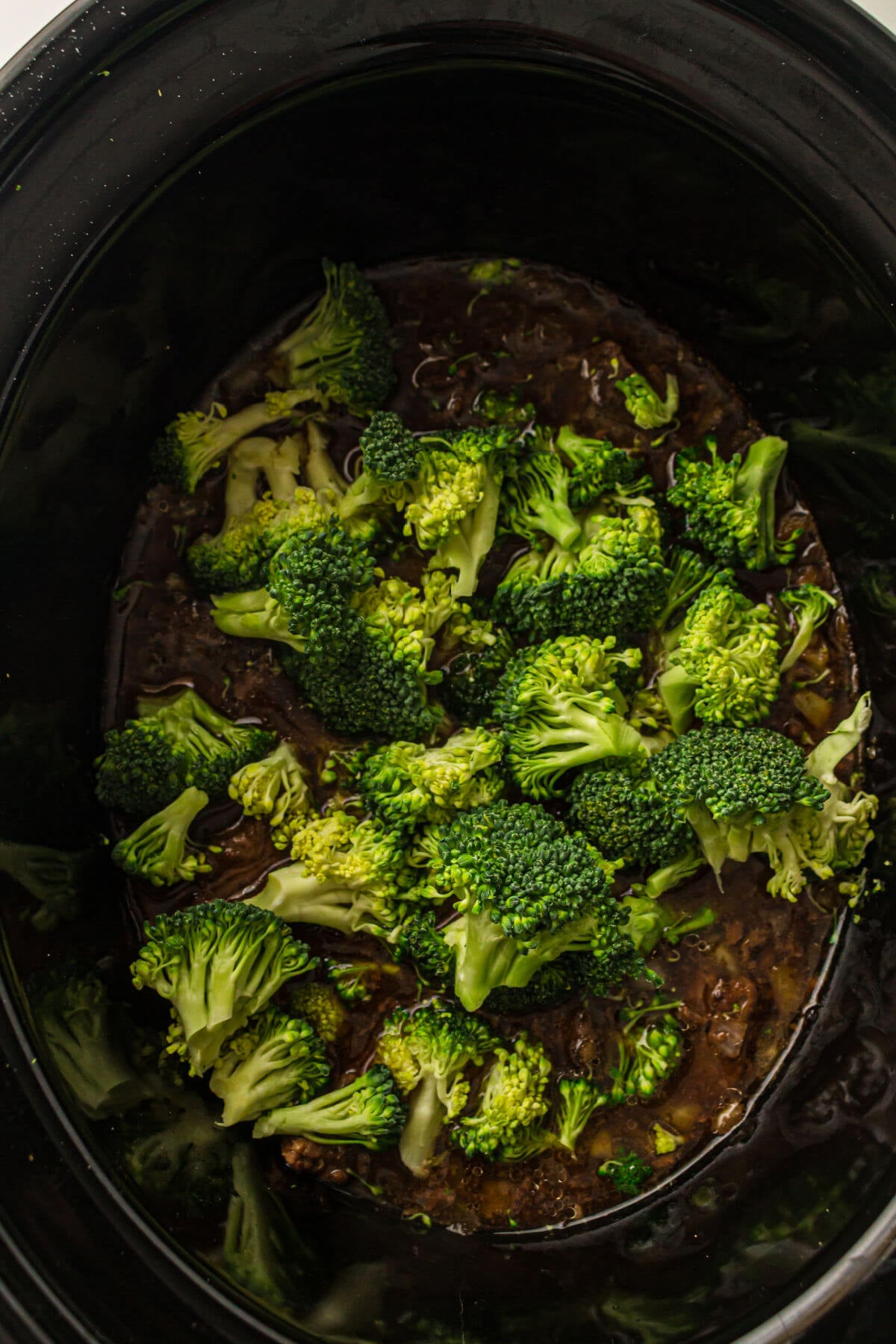 Adding broccoli to slow cooker beef and broccoli.