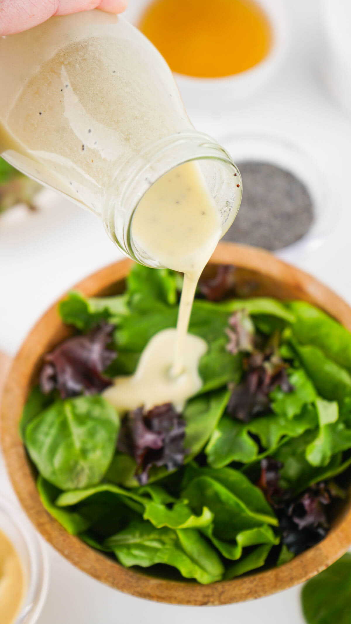Pouring homemade poppy seed dressing on a salad.