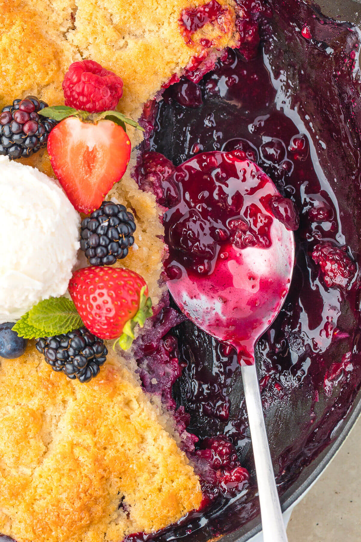 Serving sourdough mixed berry cobbler with a spoon.