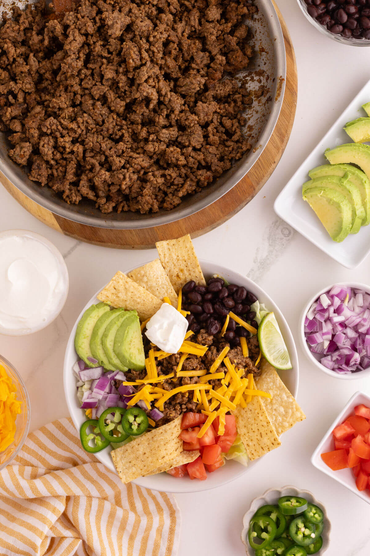 Seasoned ground beef in a skillet and easy taco salad recipe with vegetables in a bowl for serving.