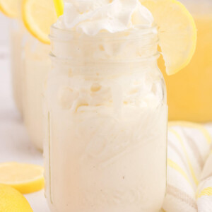 Frosted lemonade in a Mason jar with lemon wedges on the side.