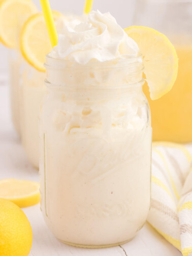 Frosted lemonade in a Mason jar with lemon wedges on the side.