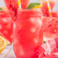 Watermelon lemonade in mason jars with a wedge of watermelon and a mint leaf on the side.
