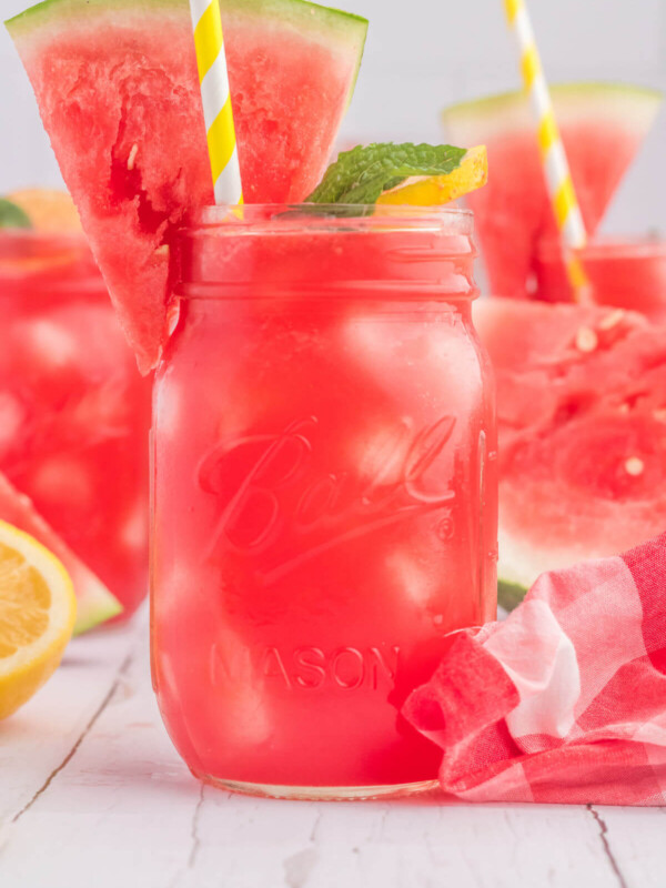 Watermelon lemonade in mason jars with a wedge of watermelon and a mint leaf on the side.