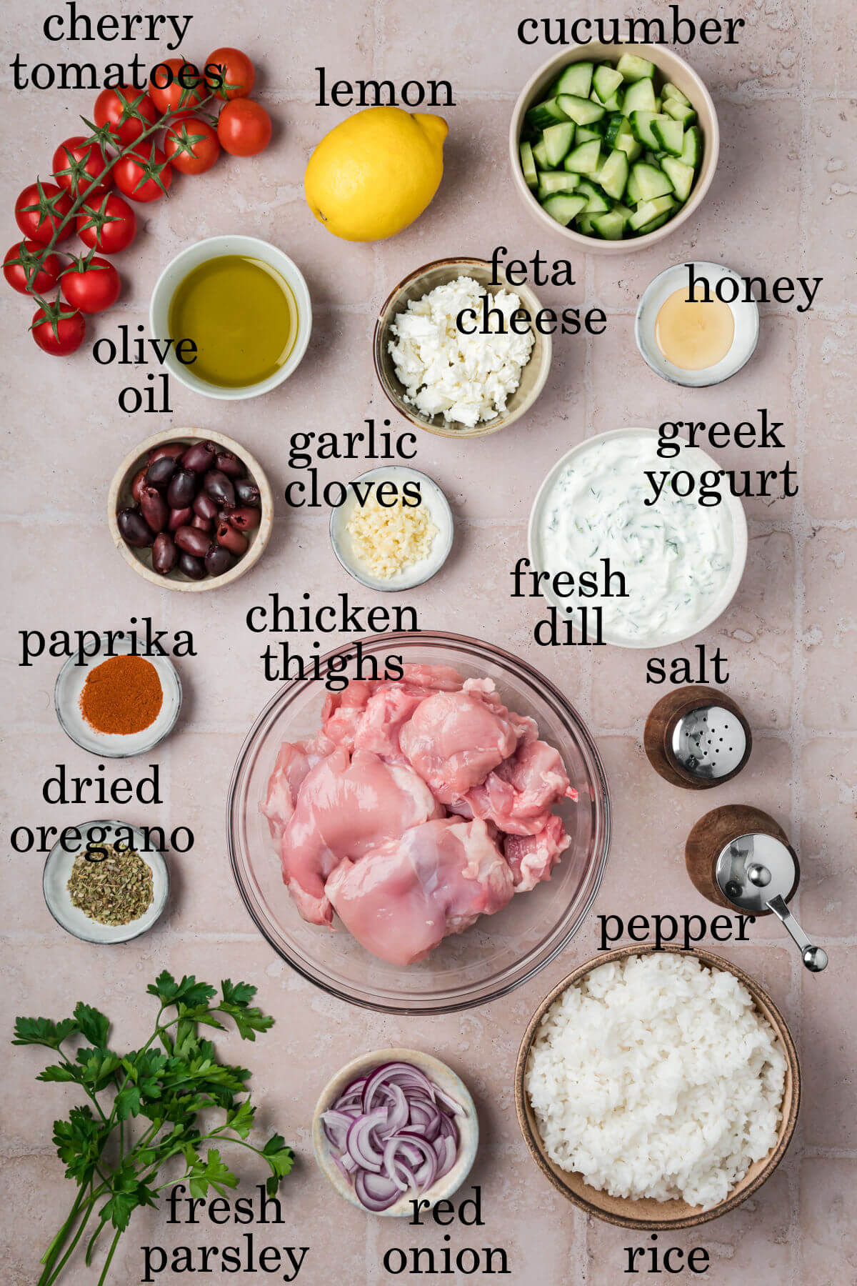 Ingredients for greek chicken bowls in small bowls with labeled text overlay labeling each ingredient.