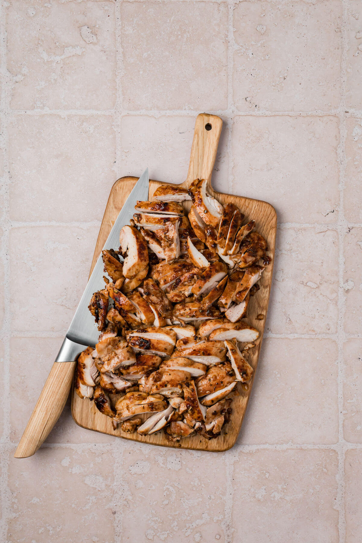 Slicing chicken on a cutting board for Greek chicken bowls.
