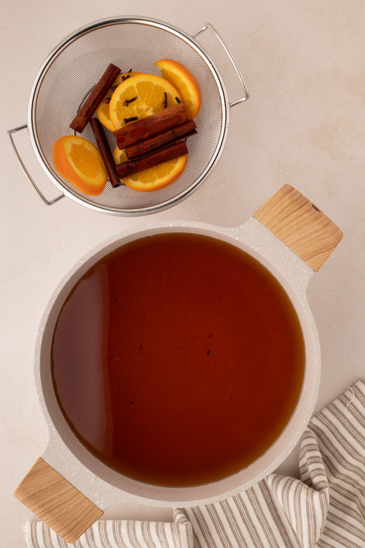 Apple juice in a pot with orange slices and other ingredients in a separate bowl.