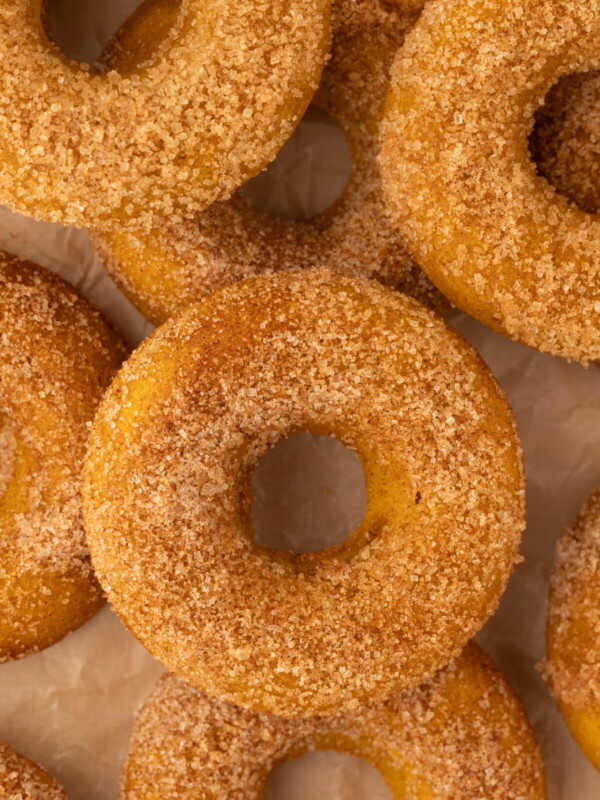 Baked pumpkin donuts in a pile on parchment paper.