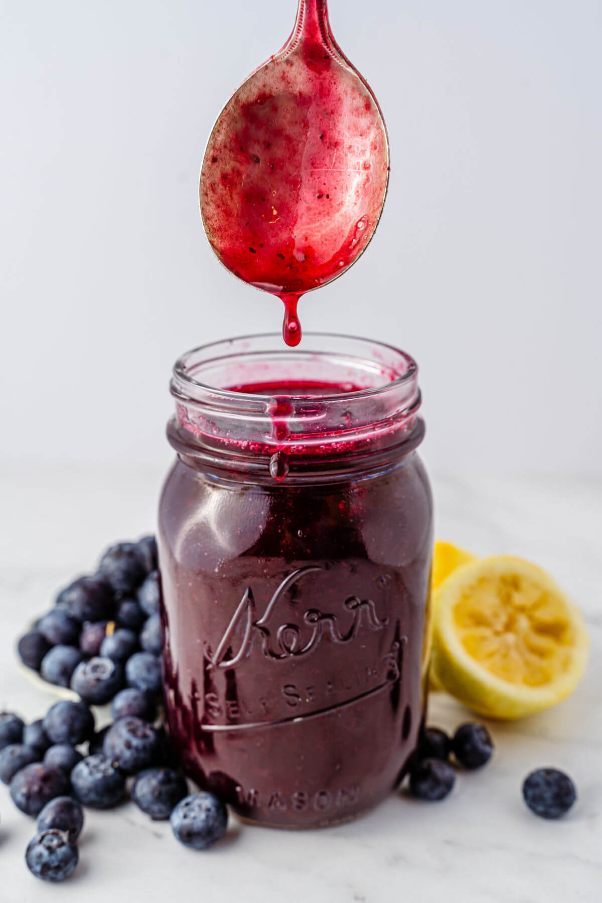 Homemade blueberry syrup in a mason jar with a spoon dipped into it.