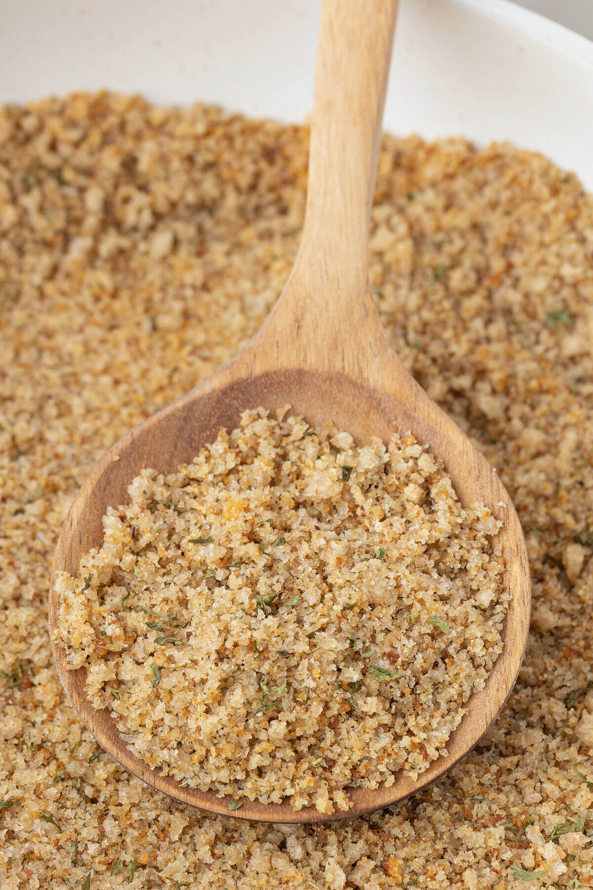 A spoon stirring seasoned breadcrumbs in a skillet.