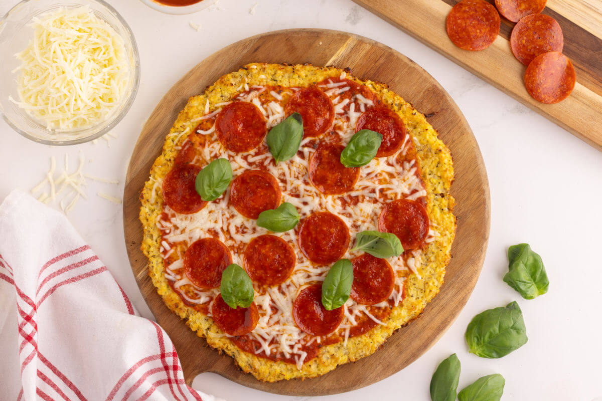 Cauliflower pizza crust on a wooden cutting board for serving.