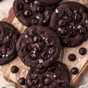 Sourdough chocolate cookies in a pile on a piece of parchment paper with some chocolate chips next to them.