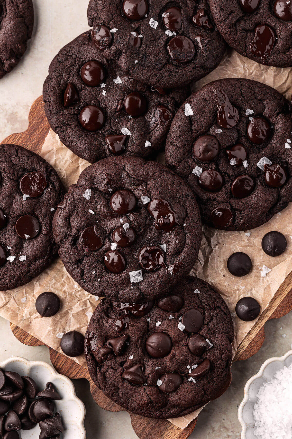 Sourdough chocolate cookies in a pile on a piece of parchment paper with some chocolate chips next to them.