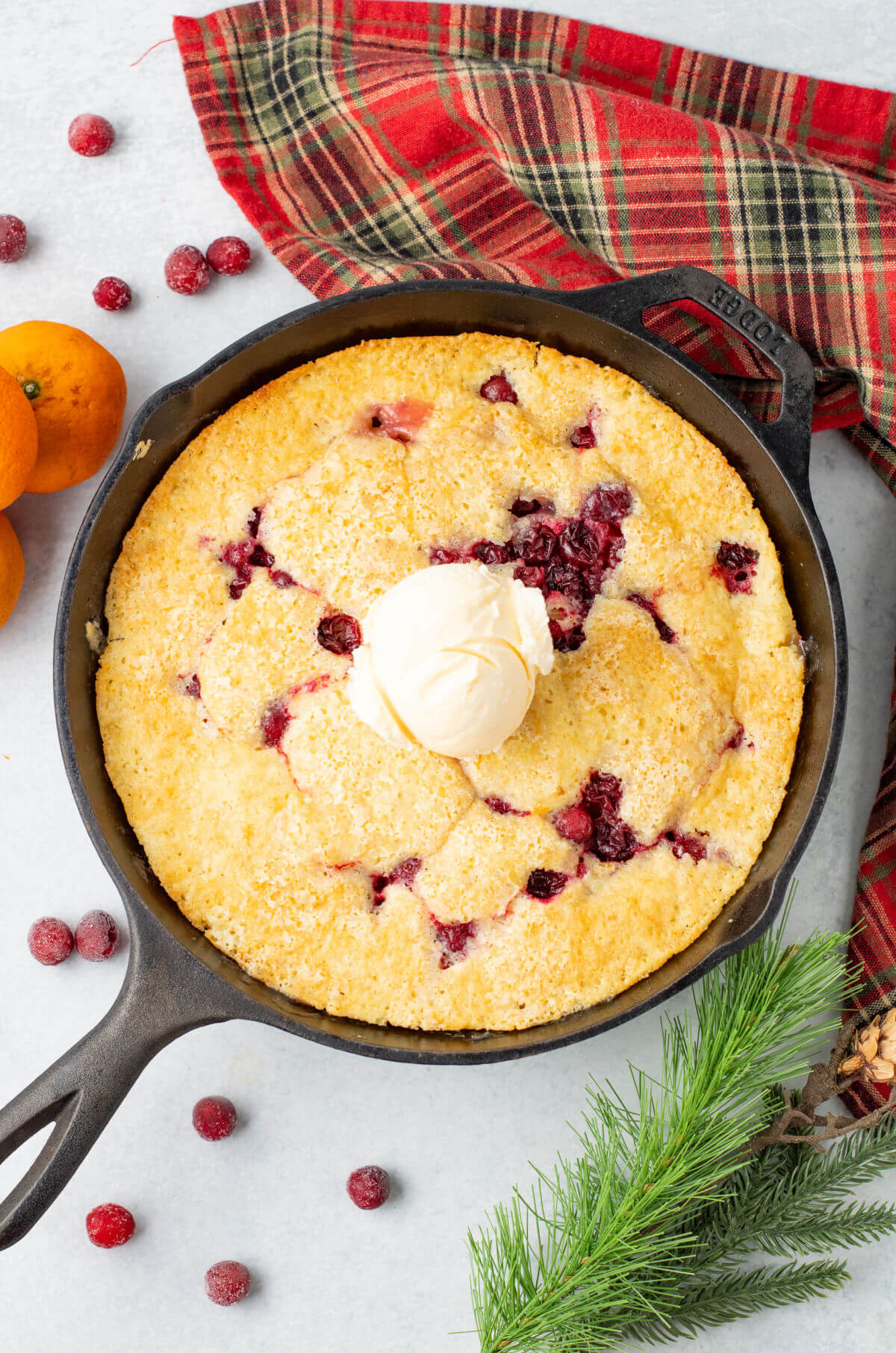 Cranberry orange cobbler in a cast iron skillet with a scoop of ice cream on top.