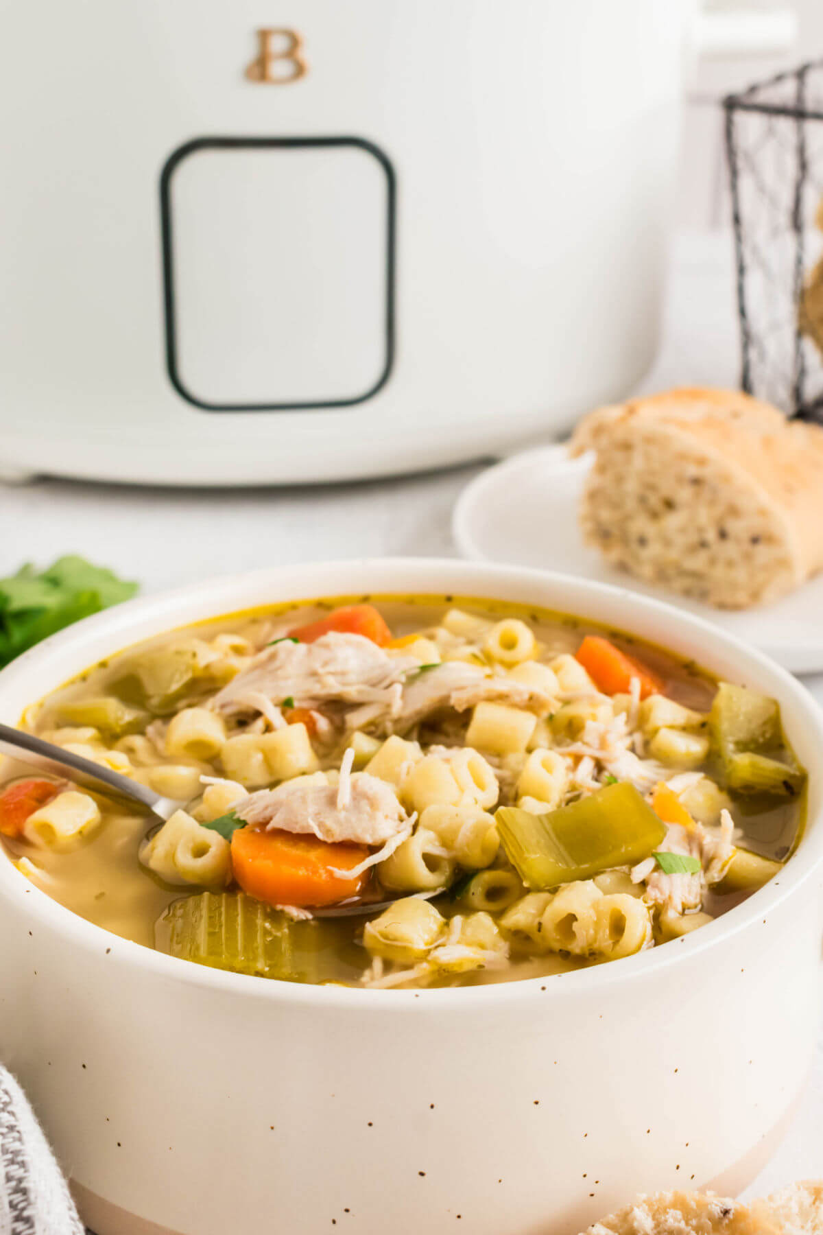 Crock Pot chicken noodle soup in a serving bowl with a slow cooker in the background.
