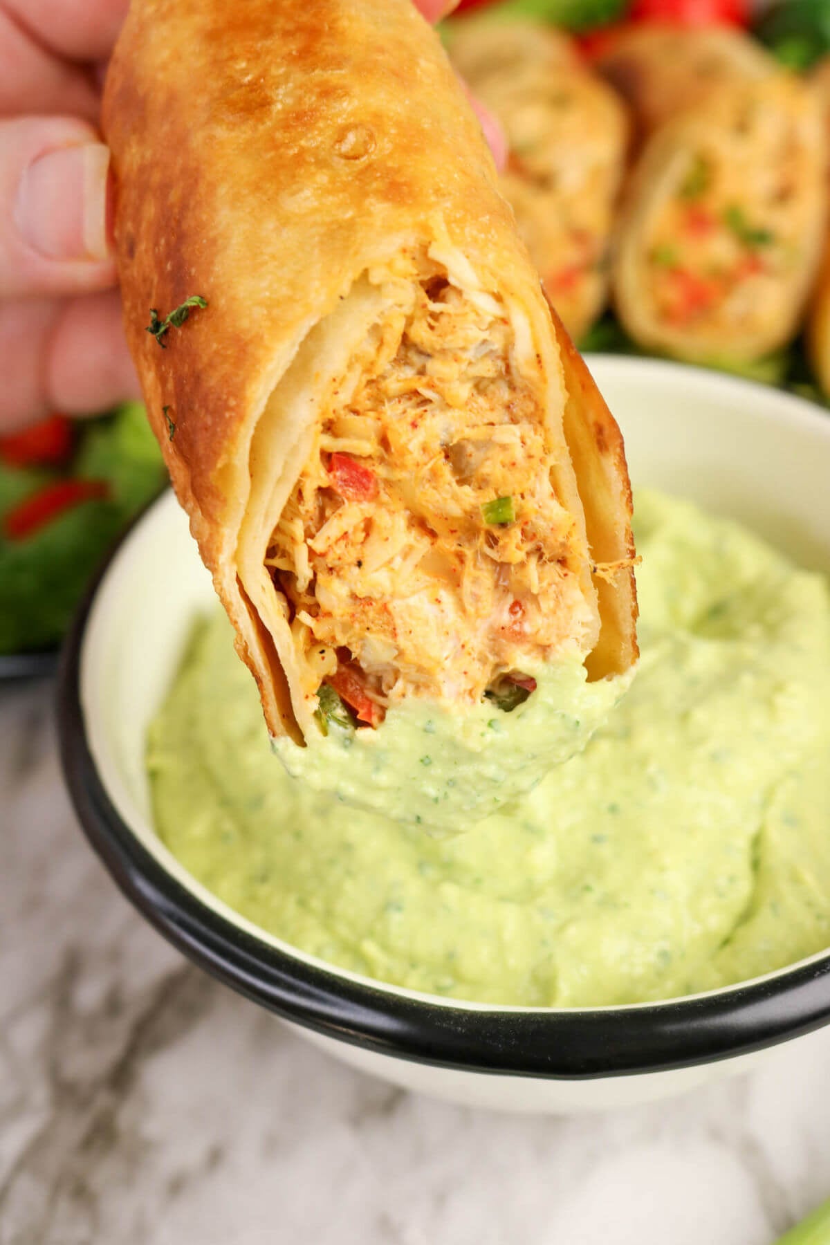 Firecracker chicken wrap being dipped into avocado lime dip.
