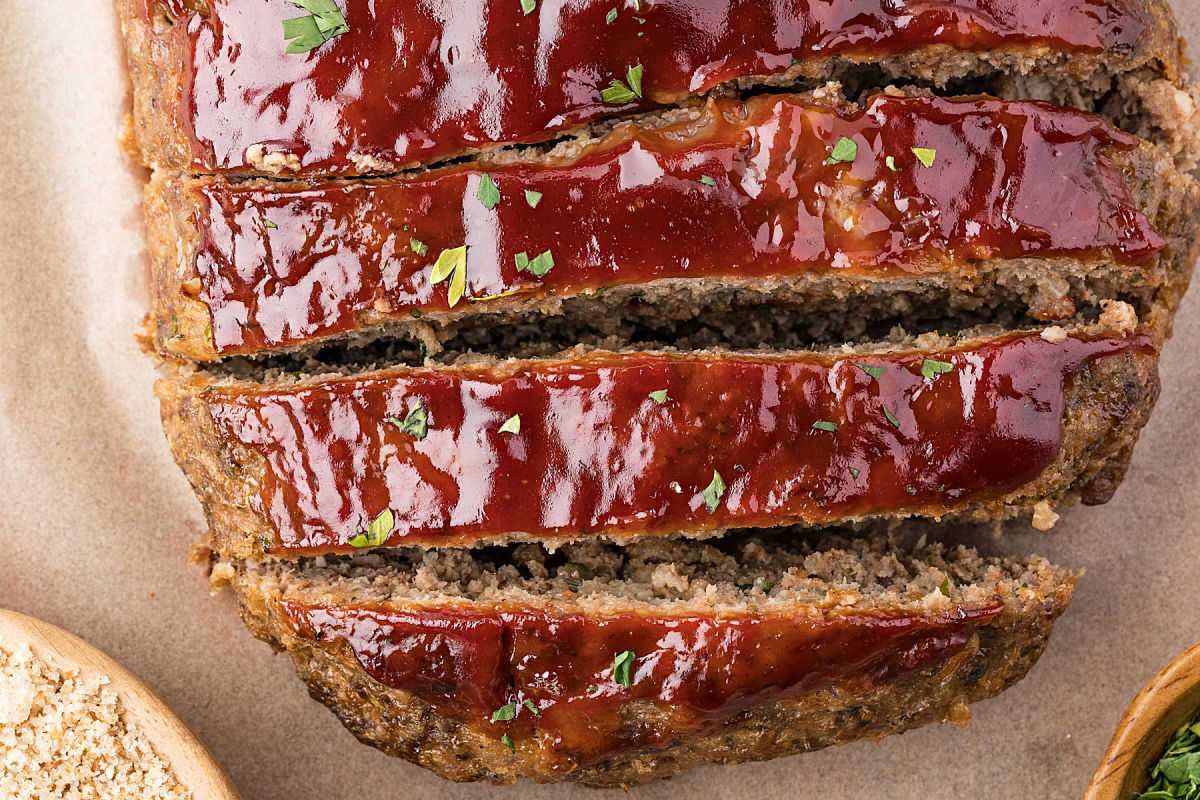 Sliced glazed meatloaf on a piece of parchment paper.