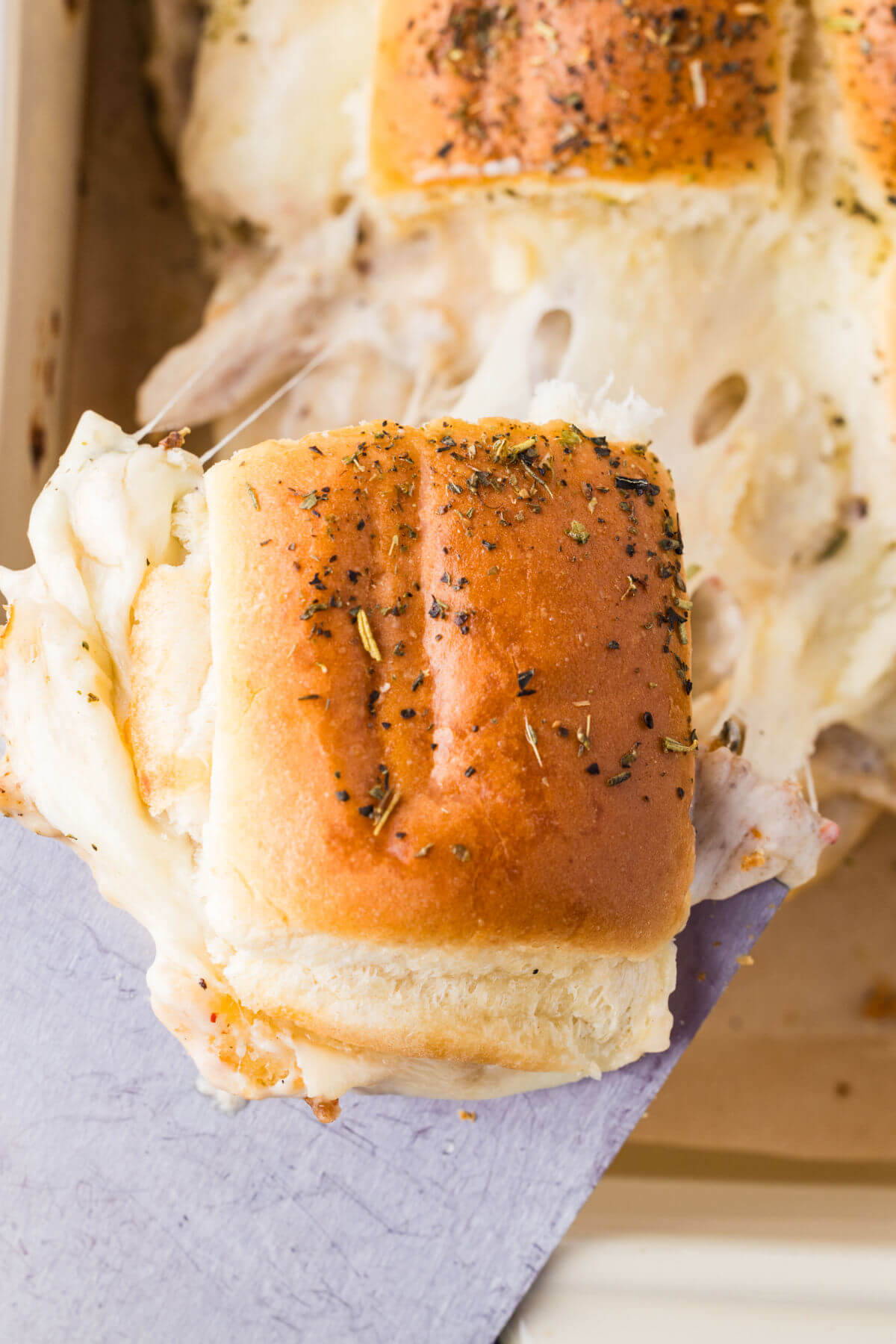 A spatula removing a marry me chicken slider from the pan, with melted cheese stretching.