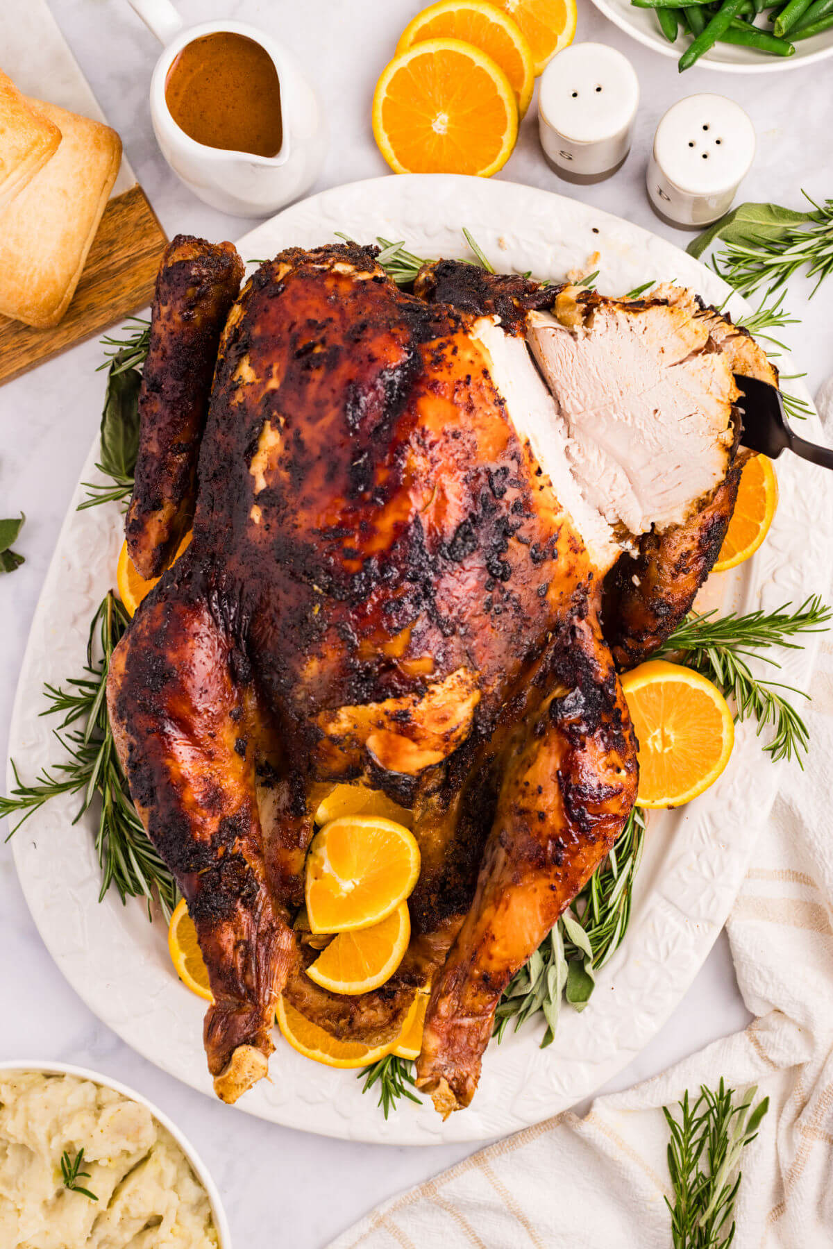 Orange glazed turkey on a white platter with herbs and orange slices.