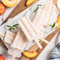 Peaches and cream popsicles on a cutting board with ice.