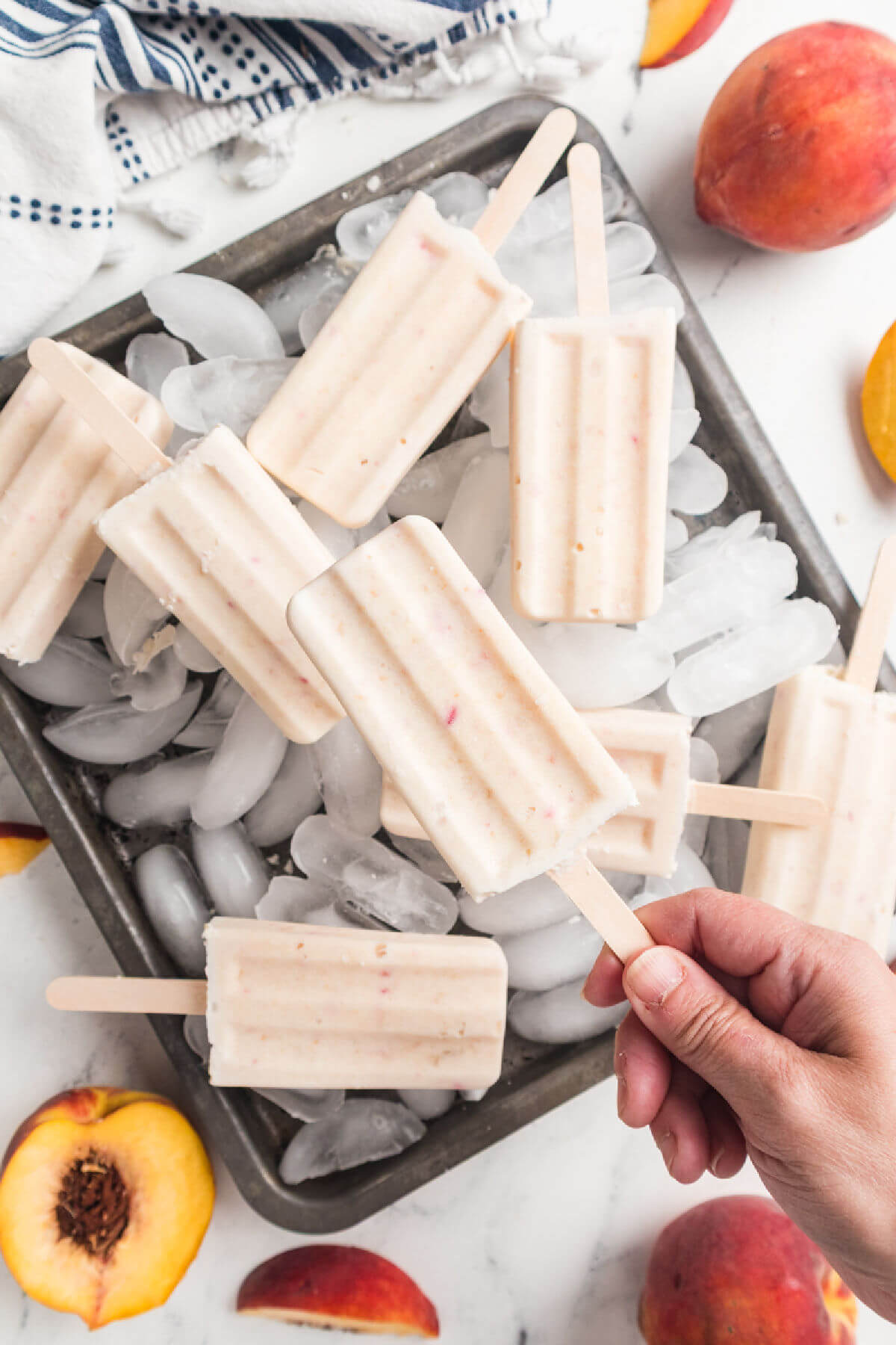 Peaches and cream popsicles on ice, with a hand holding up a popsicle.