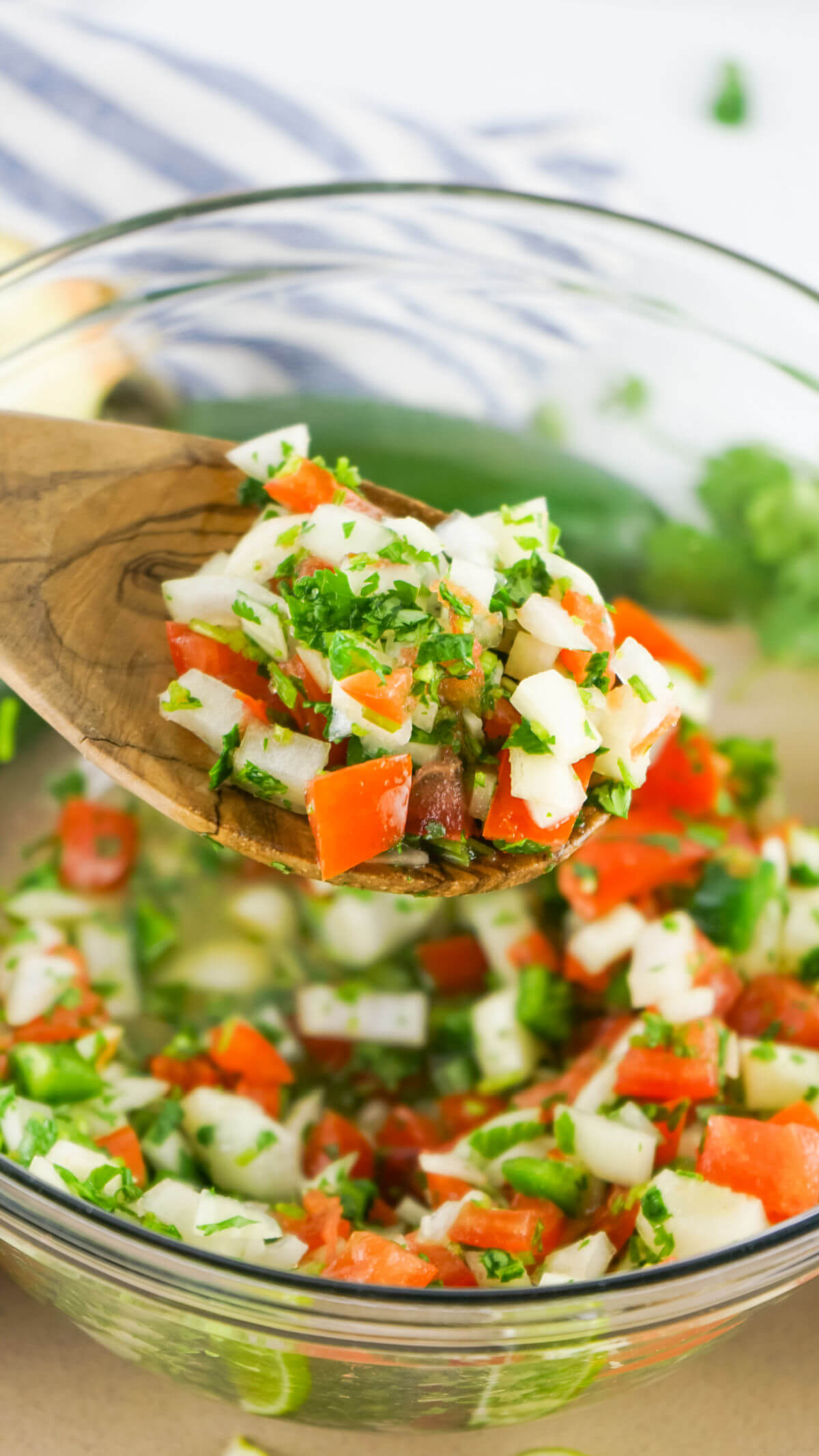 Clear bowl. with a spoon stirring pico de gallo.
